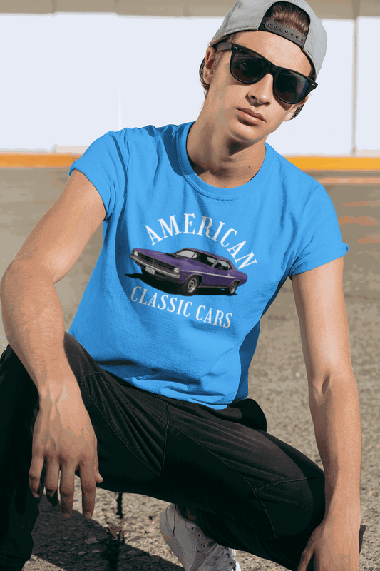 Young man wearing blue American Classic Cars Challenger graphic tee sitting outdoors in casual style