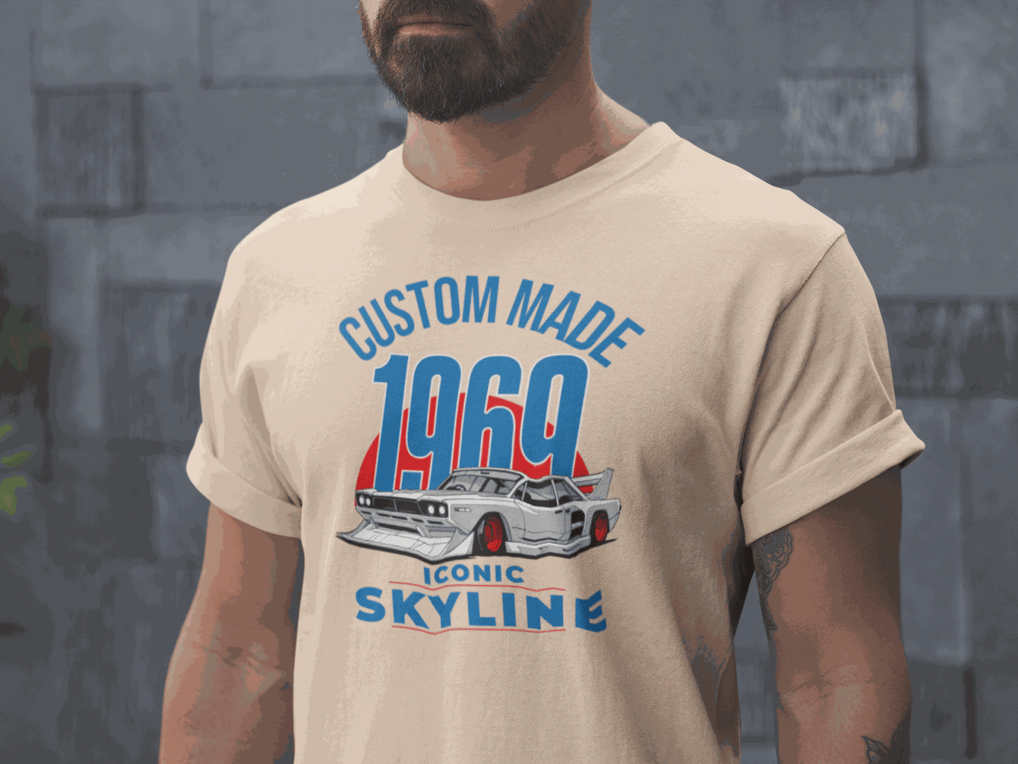 Man wearing beige Custom 1969 Iconic Skyline T-Shirt with vintage car graphic and blue-red text.
