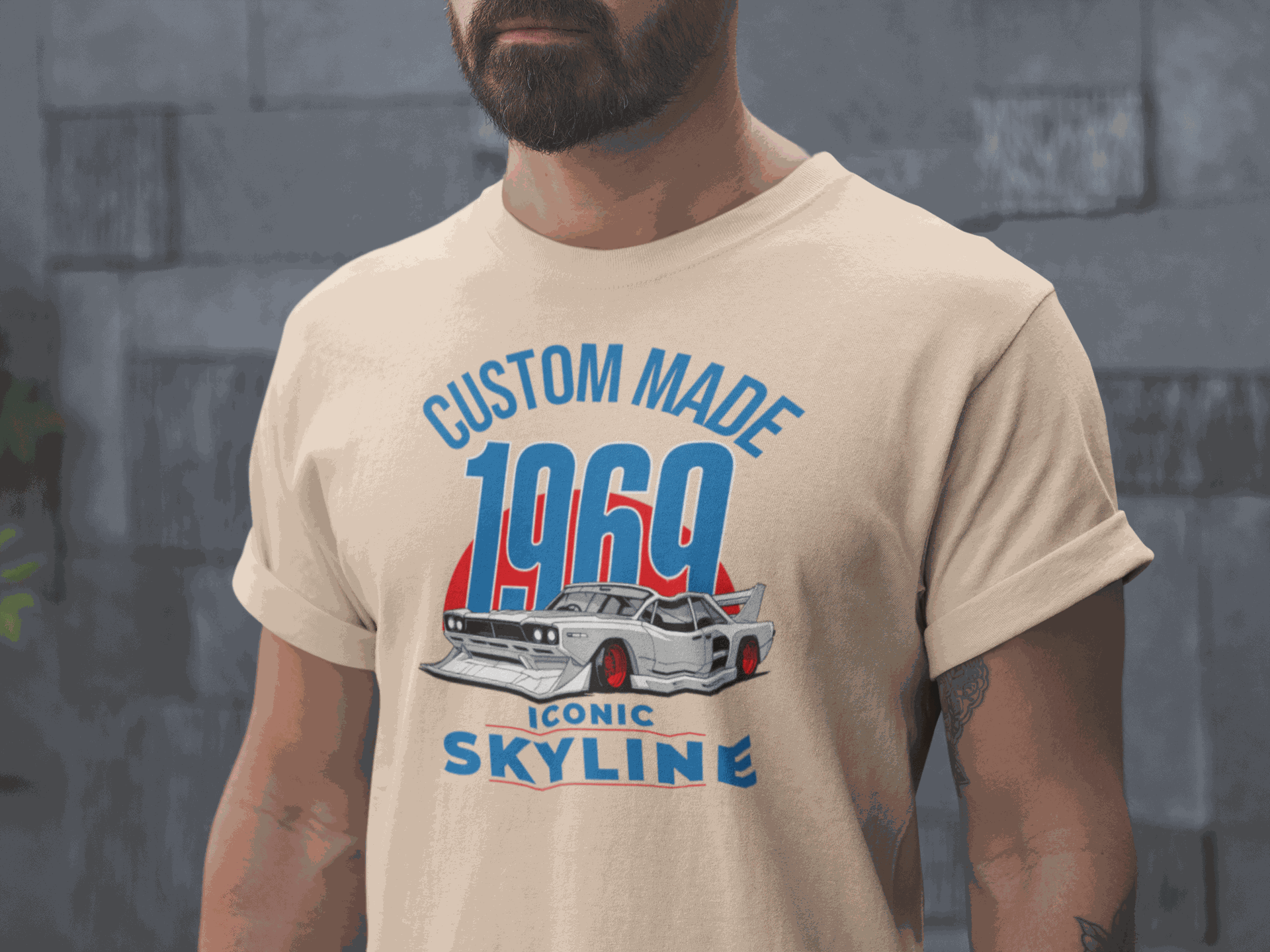 Man wearing beige Custom 1969 Iconic Skyline T-Shirt with vintage car graphic and blue-red text.